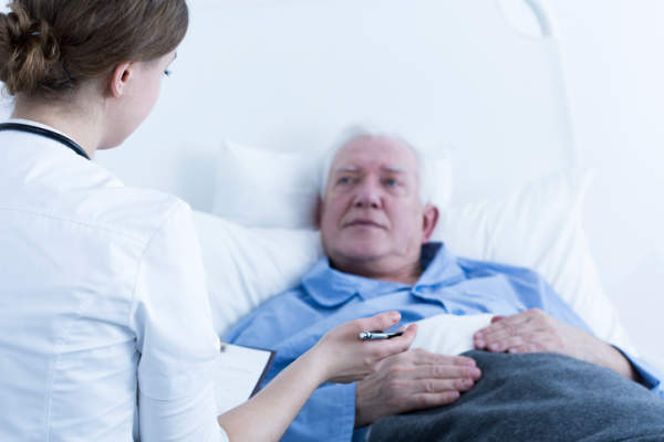 男人与护士跟他说话医院的病床上。