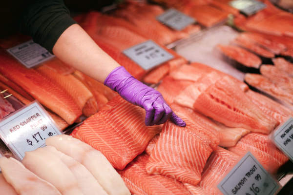 鲑鱼在市场上，戴着手套的手指着鱼片