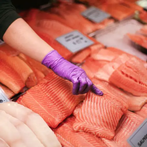 在市场上的鲑鱼，指向鱼片的手套的手