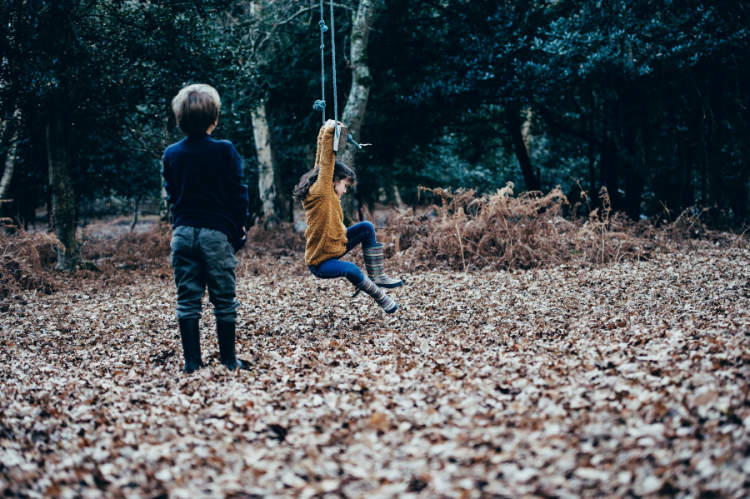 one child playing on swing, other child watching