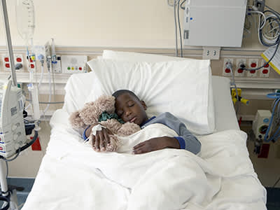抱着填充动物睡在病床上的小男孩。