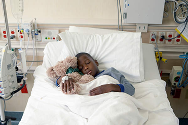 抱着填充动物睡在病床上的小男孩。