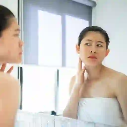 女人在镜子里看着她脸上的粉刺