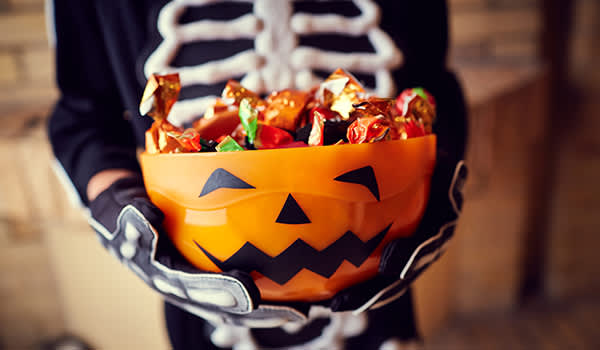 男孩穿着骷髅装,拿着装满万圣节糖果的碗。