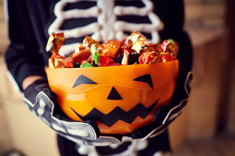 男孩骨架服装控股钵满的万圣节糖果。