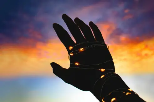 A hand with lights wrapped around it reaches towards the sky