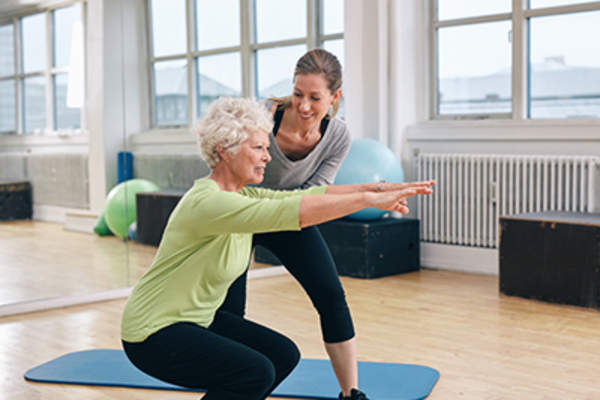 一位老妇人和她的私人教练一起做深蹲。