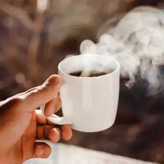hand holding steaming cup of coffee
