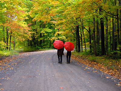 一对夫妇撑着红伞走在土路上。