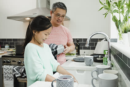 女孩和她的父亲洗碗在家里的厨房。