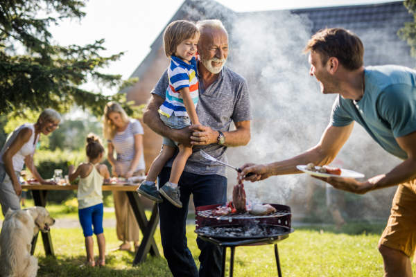 快乐的爷爷和孙子在后院和正在准备烧烤的年轻父亲聊天