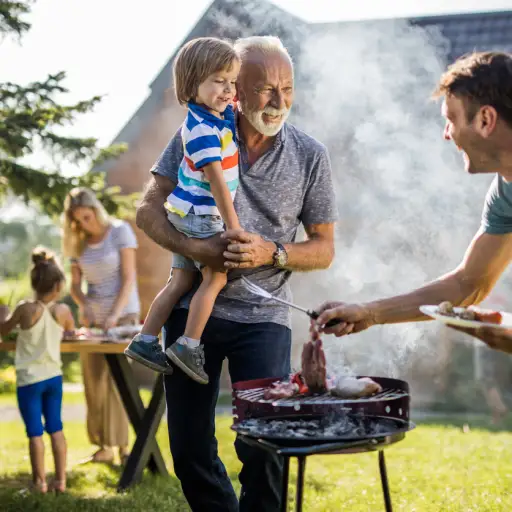 快乐的爷爷和孙子在后院和准备烧烤的小爸爸聊天