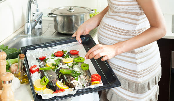 preganct妇女烹饪鱼和蔬菜的形象