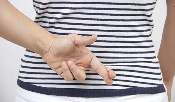 Woman with blue and white striped shirt with fingers crossed behind her back.