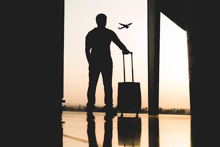 男子的剪影与手提箱看着飞机