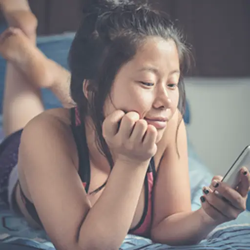 Woman lying on bed and using mobile phone.