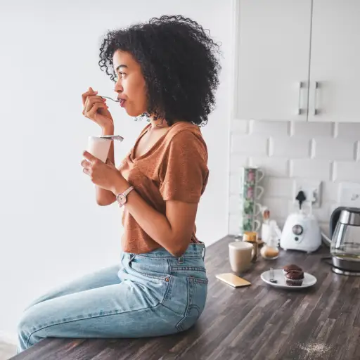 年轻女子坐在厨房柜台上吃酸奶。
