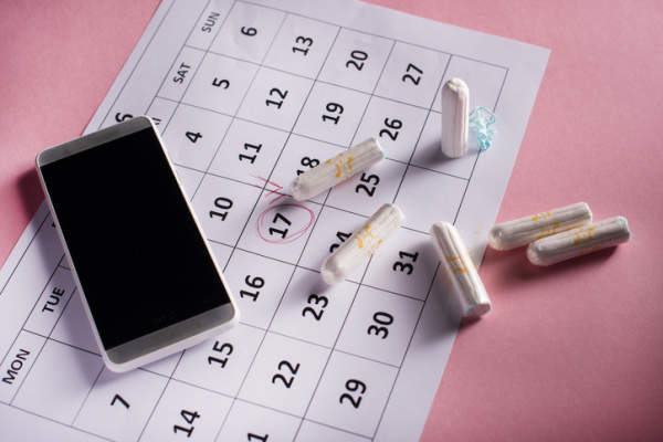 干净的白色卫生棉条，日历和手机上的粉红色背景