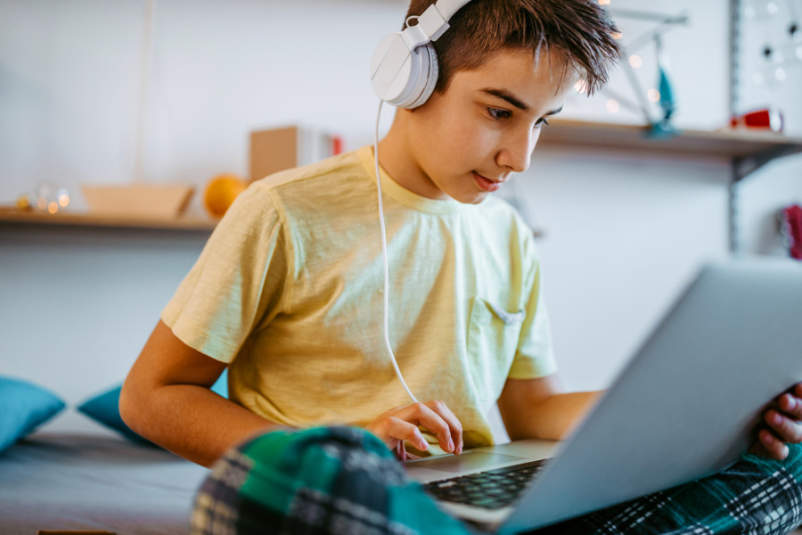 十几岁的男孩用耳机使用在卧室里一台笔记本电脑