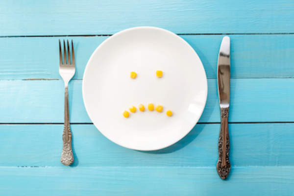 8个皱着眉头的玉米小丸子,放在白色的餐盘上,放在刀叉之间。