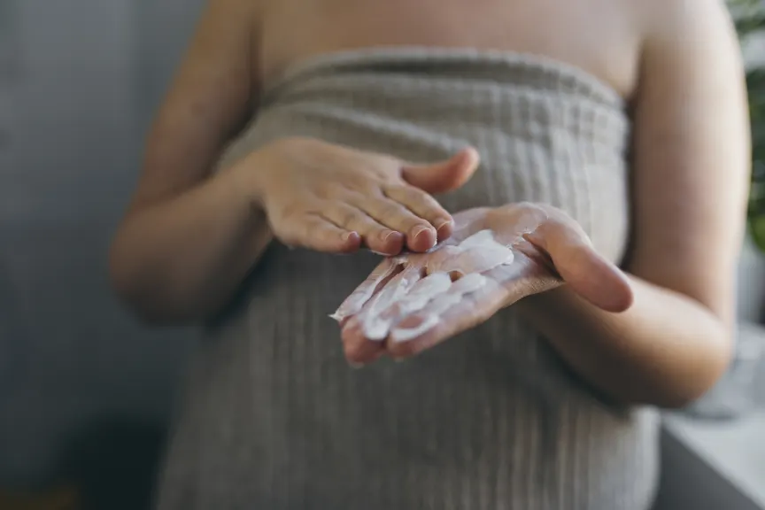 女人裹着毛巾穿上浴后乳液。
