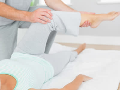 理疗师帮助年轻女子做膝伸展运动。