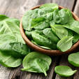 Fresh baby spinach leaves in a bowl on a wooden table