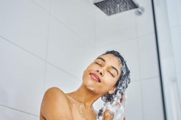 年轻女子洗她的头发用洗发水在淋浴