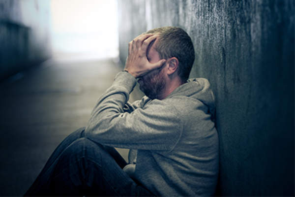 无家可归的人坐在那里,双手抱着头。