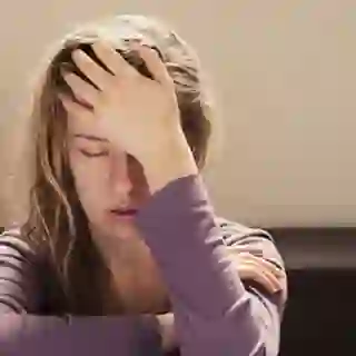 Hypersensitive young woman with eyes closed, hands on head.