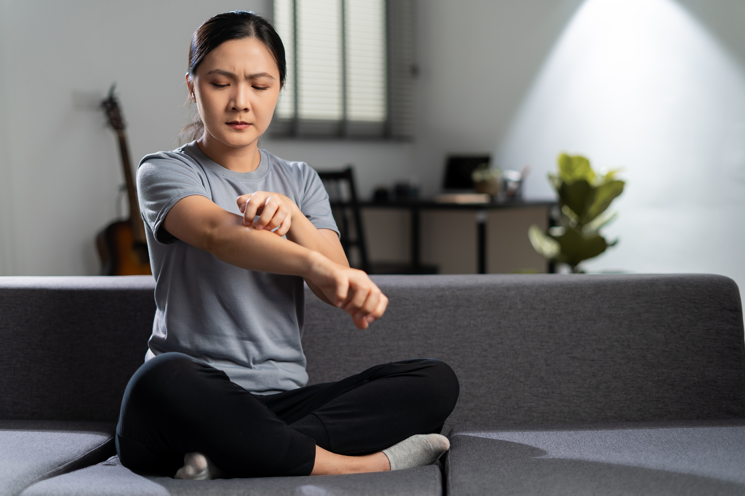 woman scratching her skin, sitting on sofa in living room at home