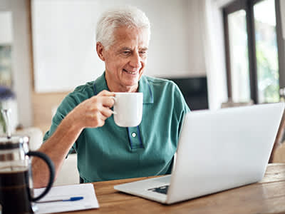 而在家里笔记本电脑微笑的人控股咖啡。