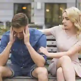 Woman comforting her distressed boyfriend on a bench.