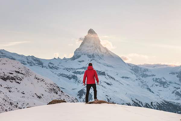 穿红夹克的男人站在雪地里望着远方的山