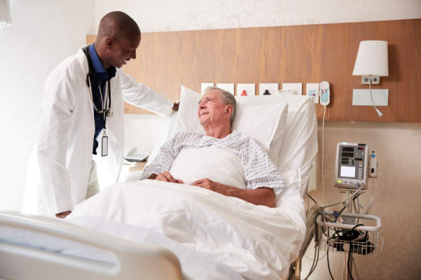 医生访问和谈话与高级男患者在医院的床