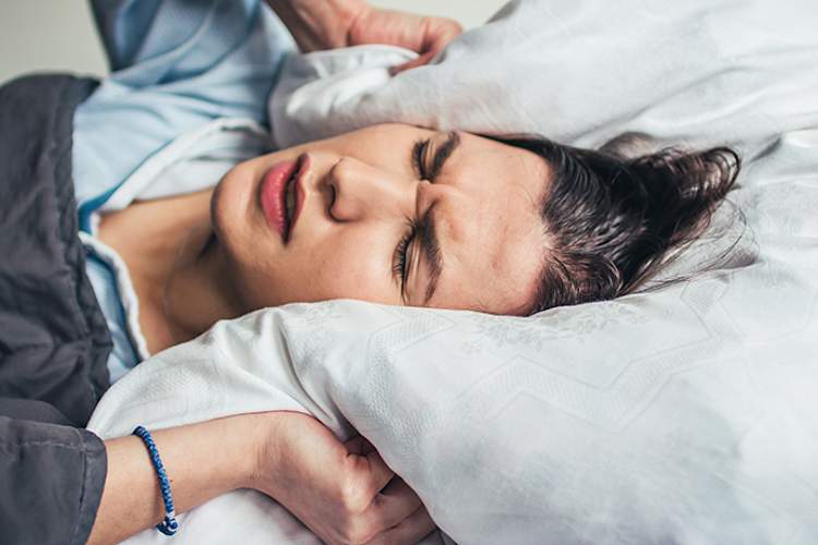 女人失眠捂住耳朵用枕头。