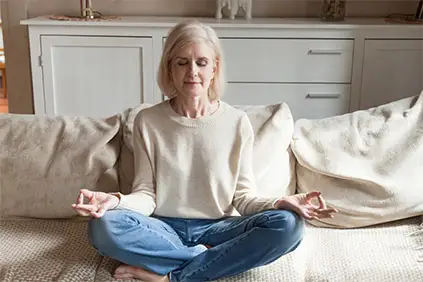 Woman meditating at home on couch.