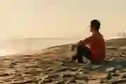 A man sits on a beach and watches the sunset
