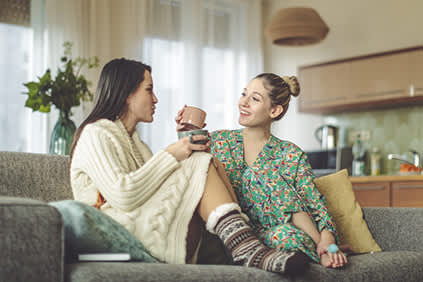 两个年轻女子穿着睡衣在沙发上喝咖啡。