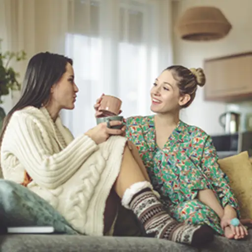 两个穿着睡衣的年轻女人在沙发上喝咖啡。