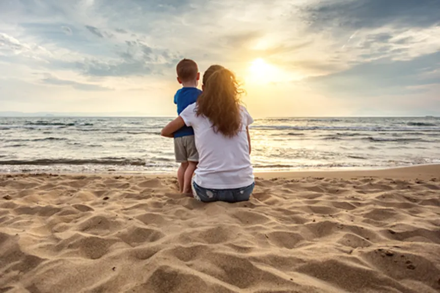 Mother and young son watching sunset on the beach.