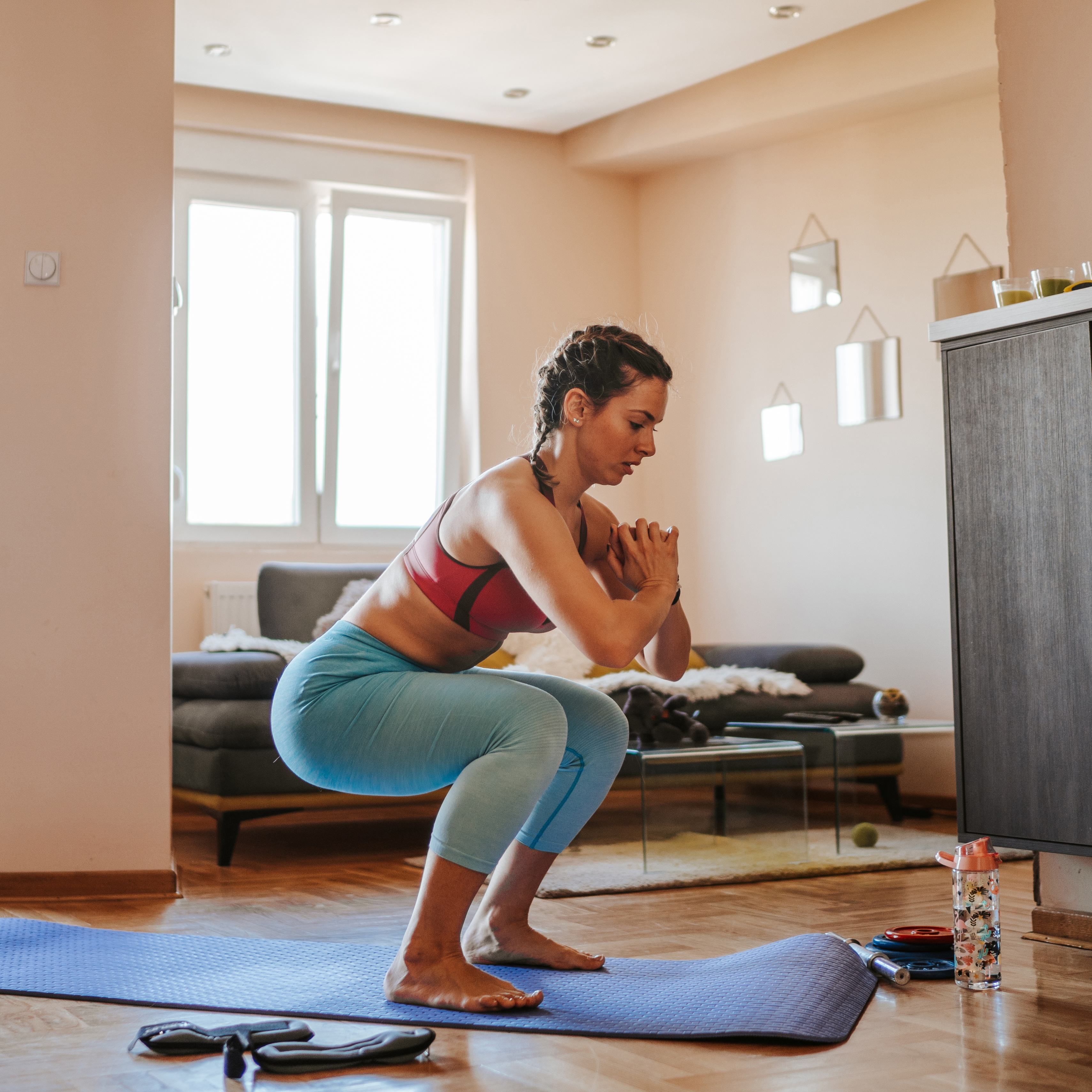 年轻女子在客厅的瑜伽垫上做深蹲