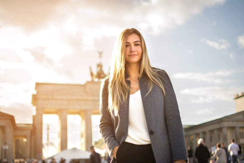 德国柏林，一位微笑的时尚年轻女子站在布兰登伯格面前。