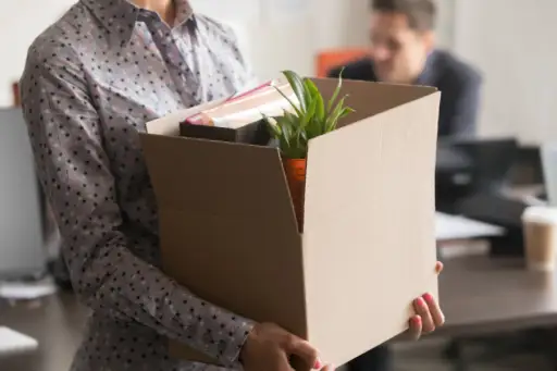 employee carrying cardboard box of her stuff out of an office