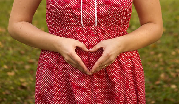 妊娠头三个月，手在肚子心脏的形状中的女人。