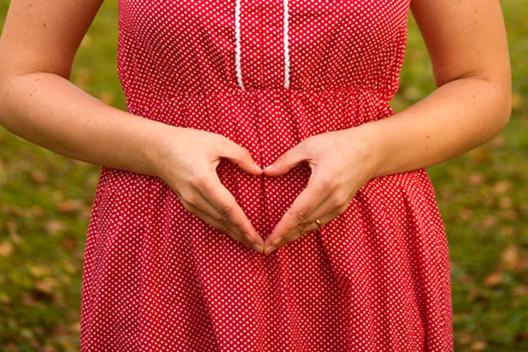 女人在怀孕头三个月,我的手n shape of heart over stomach.