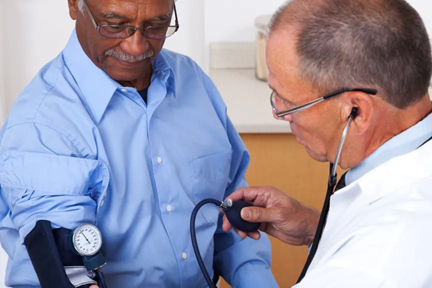 Doctor taking older man's blood pressure in office.