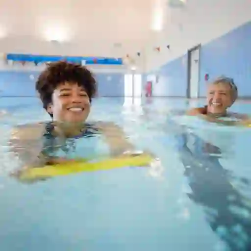 两名妇女在室内游泳池中用踢腿板游泳时微笑着。