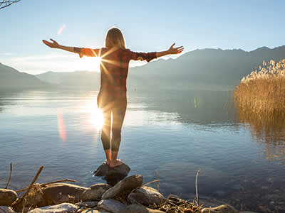 女人站在岩石附近美丽的高山湖泊外展双臂。