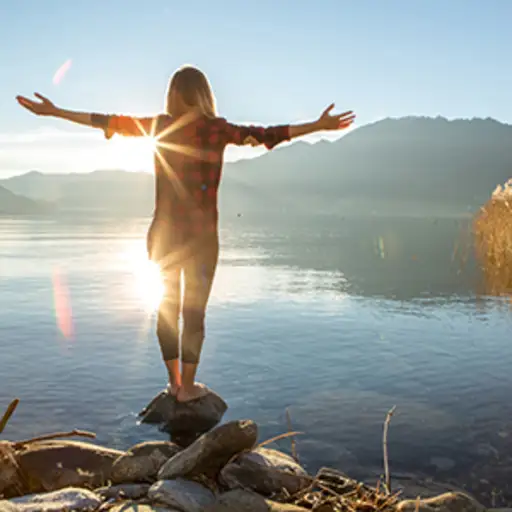 一个女人站在岩石上伸出双臂，靠近美丽的山湖。